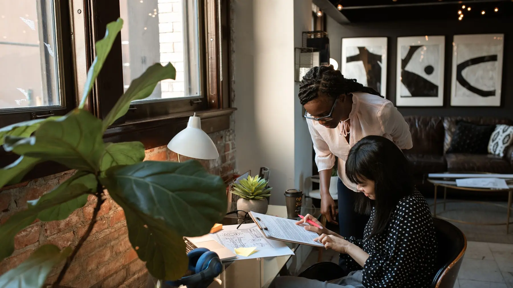 Duas pessoas sentadas à mesa de um escritório revisando papéis juntas, no meio de uma conversa de trabalho
